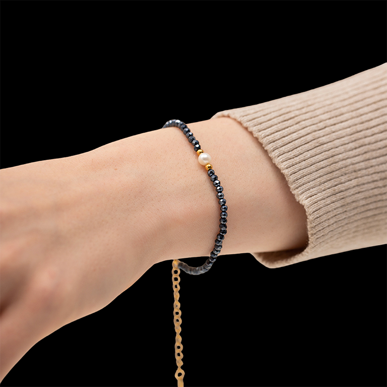 Close-up of a wrist wearing a beaded bracelet with a black and gold chain on a black background