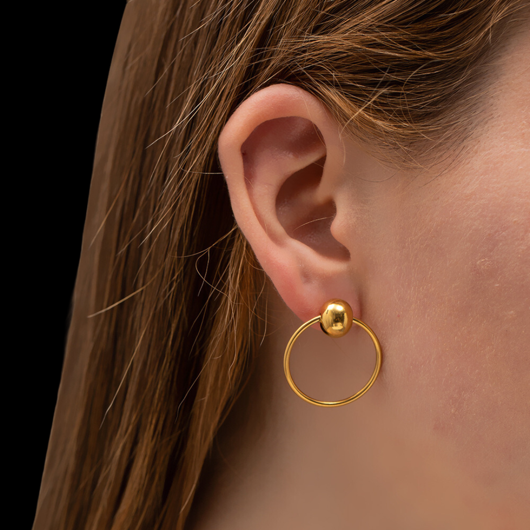 Gold hoop earring worn by a person with a black background
