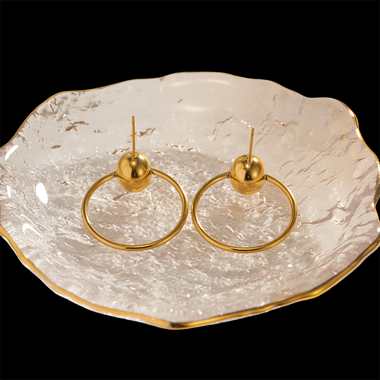 Gold hoop earrings on a textured white dish with gold rim against a black background